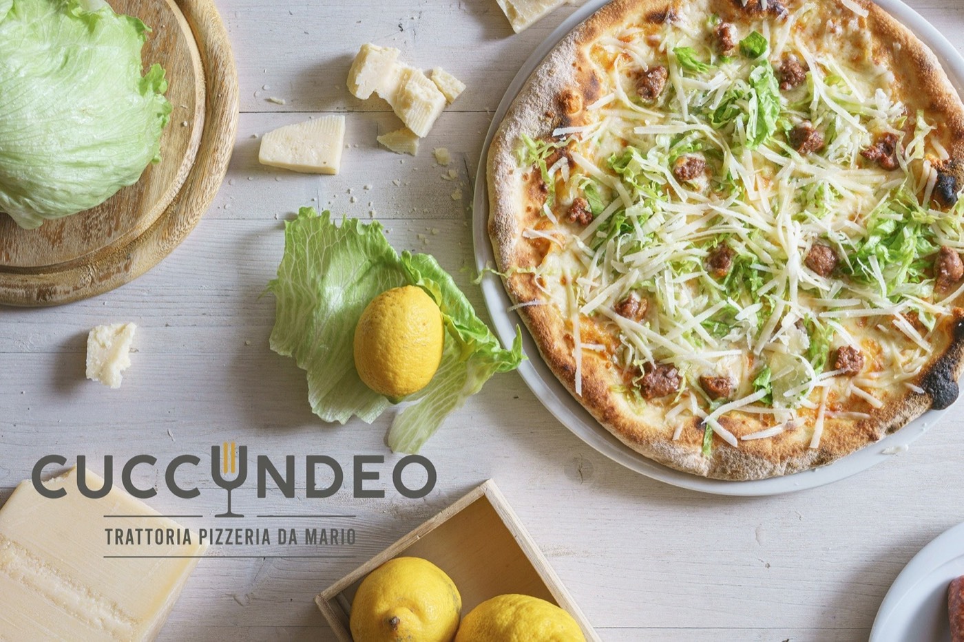 Une pizza aux légumes et saucisse sur la table blanche, à côté de citrons et de fromage